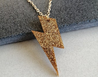 May include: A gold glitter lightning bolt pendant necklace on a silver chain.
