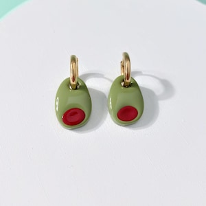 K&ouml;nnte beinhalten: Olivenf&ouml;rmige Ohrringe. Jeder Ohrring hat ein gr&uuml;nes Oval mit einem roten Kern, das einer Olive &auml;hnelt. Die Ohrringe h&auml;ngen an goldfarbenen Creolen und sind ein verspieltes und einzigartiges Accessoire.