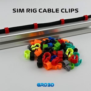 以下が含まれることがあります： ワイヤーやケーブルを整理するためのカラフルなケーブルクリップの山。クリップはプラスチック製で、赤、緑、青、黄、オレンジ、黒など、さまざまな色があります。クリップはさまざまなケーブルサイズで使用できるように設計されており、ケーブルを整理して整頓するために使用できます。  SIM RIG CABLE CLIPSとGRD3Dが画像に印刷されています。