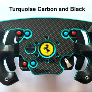 Pode incluir: Um volante de corrida preto e turquesa com detalhes em fibra de carbono. O volante apresenta botões com as etiquetas "FLASH", "RADIO" e "WATER". O centro exibe um logótipo amarelo da Ferrari. O texto "Turquoise Carbon and Black" está no topo.