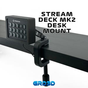 May include: Black Stream Deck MK2 desk mount with a clamp to attach to a desk or table. The mount is made of plastic and has a black finish. The Stream Deck MK2 is a popular device for streamers and content creators.