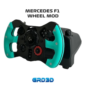 May include: A black and teal racing wheel mod for a Logitech G29 or G920 racing wheel. The mod features a carbon fiber look and a teal leather-like grip. The text "MERCEDES F1 WHEEL MOD" is printed above the wheel. The text "GRD3D" is printed below the wheel.