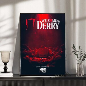 May include: Framed poster with a dark red background featuring the text "IT" and "WELCOME TO DERRY" in white. The poster also includes the HBO Max logo and the phrase "NOW STREAMING".