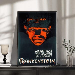May include: Framed vintage poster featuring a striking orange and black image of Frankenstein's monster. The poster includes the text "WARNING! THE MONSTER IS LOOSE! FRANKENSTEIN" in a bold, eye-catching font. A classic horror movie theme.