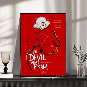 Könnte beinhalten: Gerahmtes Poster mit rotem Hintergrund, das eine Illustration aus "Der Teufel trägt Prada" zeigt. Das Kunstwerk zeigt eine Frau mit weißem Haar und rotem Mantel. Der Filmtitel ist in weißem und schwarzem Text.