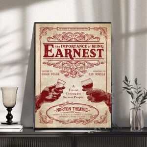 Könnte beinhalten: Gerahmtes Vintage-Poster mit dem Titel "The Importance of Being Earnest" in roter Schrift. Das Poster zeigt Illustrationen von Händen, die Gläser mit Wein und Likör halten. Es ist eine Werbung für ein Comedy-Stück.