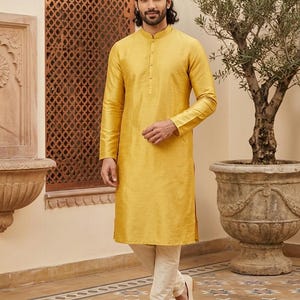 Könnte beinhalten: Senfgelbes Kurta mit Stehkragen und langen Ärmeln. Das Kurta wird mit cremefarbenen Hosen und cremefarbenen Loafern kombiniert. Das Outfit eignet sich für formelle oder festliche Anlässe.