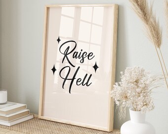 May include: A framed print with the text "Raise Hell" in black cursive font on a light pink background. The print is hanging on a wall above a light wood bench with a woven rattan top. There are two woven baskets on the floor in front of the bench and a vase with dried white flowers on the bench.
