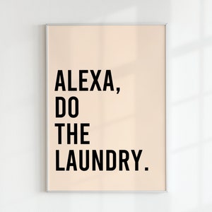 May include: A framed print with a light peach background and black text that reads "ALEXA, DO THE LAUNDRY."