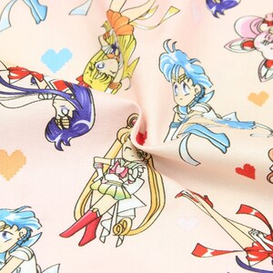May include: Pink fabric with a repeating pattern of cartoon characters from the anime Sailor Moon. The characters are in various poses and are wearing their signature outfits. The background is a light pink with small white hearts.