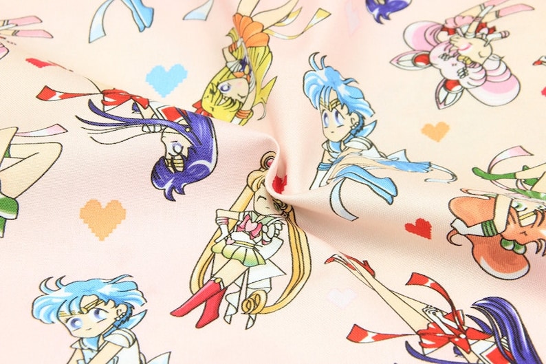 May include: Pink fabric with a repeating pattern of cartoon characters from the anime Sailor Moon. The characters are in various poses and are wearing their signature outfits. The background is a light pink with small white hearts.