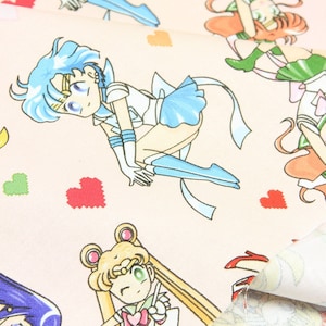 May include: Pink fabric with a repeating pattern of anime characters in various poses. The characters are wearing sailor outfits with different colored accents. The fabric is decorated with small hearts.