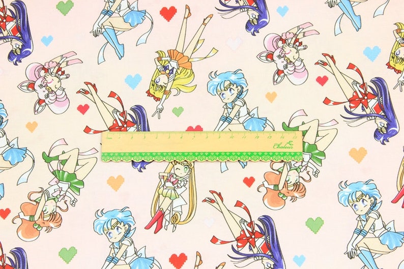 May include: A pink fabric with a repeating pattern of Sailor Moon characters. The characters are in various poses and are wearing their signature outfits. The background is a light pink with small hearts.