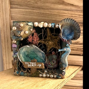 May include: A small wooden box decorated with seashells, starfish, and a seahorse. The box has a sign that says "To the Beach" with an arrow pointing to the right.