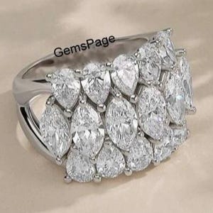 Könnte beinhalten: Ein silberner Ring mit einer Ansammlung klarer, birnenförmiger und marquiseförmiger Edelsteine. Der Ring hat ein breites Band und die Edelsteine sind in einem geschichteten Muster angeordnet. Der Text "GemsPage" ist sichtbar.