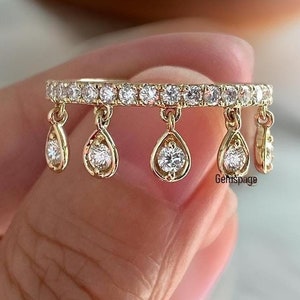 Könnte beinhalten: Ein goldener Ring mit einer Reihe kleiner Diamanten und fünf baumelnden birnenförmigen Diamanten.