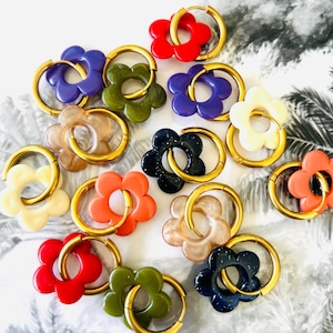 Peut inclure: Un ensemble de 12 boucles d'oreilles créoles dorées avec des breloques de fleurs colorées. Les breloques sont de différentes couleurs, notamment rouge, orange, jaune, vert, bleu, violet et blanc.