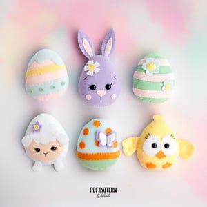Könnte beinhalten: Eine Sammlung handgefertigter Osterdekorationen aus Filz, darunter Eier, ein Hase, ein Lamm und ein Küken. Die Dekorationen sind in Pastellfarben mit Blumen- und Schmetterlingsakzenten gehalten. Der Text "PDF PATTERN by belarba" befindet sich unten.