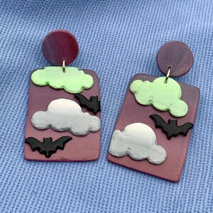 May include: A pair of purple and green Halloween-themed earrings with a cloud and bat design.