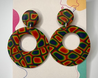 Puede incluir: Un par de pendientes de aro estampados y coloridos. Los pendientes tienen un diseño circular con un círculo más pequeño en la parte superior. El patrón es una mezcla de rojo, amarillo, verde y azul. Se muestran en una tarjeta con el texto "DREAM JUNK STUDIO Handcrafted in Bristol."