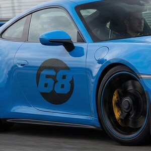 May include: A vibrant blue sports car featuring a black and carbon fibre number 68 decal on the door. The car has black wheels with blue accents and yellow brake calipers. The side mirror is blue.