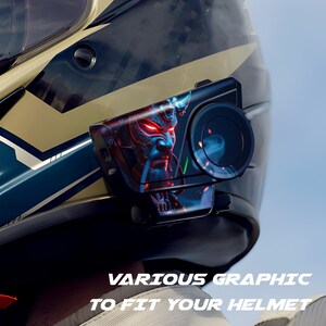 May include: A black motorcycle helmet with a graphic of a blue and red demon face. The helmet has a camera attached with a circular lens. The text "VARIOUS GRAPHIC TO FIT YOUR HELMET" is at the bottom.