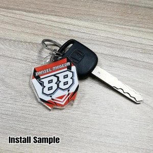 May include: A red, white, and black acrylic keychain with the text "Daniel Mogeda" and the number "88" in white. The keychain is attached to a silver key ring.