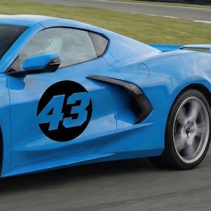 May include: A bright blue sports car with a black circle and the number 43 on the side. The car has a sleek design with a spoiler and silver rims. The wheels are in motion.