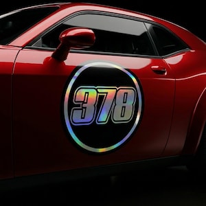 May include: A red car with a black and iridescent sticker on the side. The sticker is a circle with the number "378" in a bold, stylized font. The car's side mirror is visible.