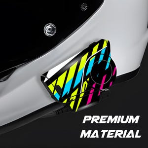 Puede incluir: Casco de moto blanco con visera negra. Un dispositivo de comunicación está fijado en el lateral, con un diseño colorido de rayas amarillas, azules y rosas. El texto "PREMIUM MATERIAL" se muestra debajo.