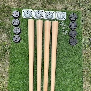 Op de afbeelding: Vier houten tafelpoten met metalen bevestigingsplaten, zwarte kunststof voeten en kurken pads. De poten zijn in een rij op een groene kunstgras ondergrond geplaatst.