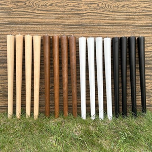 Peut inclure: Un ensemble de 12 pieds de table en bois de différentes couleurs, dont le bois naturel, le brun, le blanc et le noir. Les pieds sont tous de la même taille et de la même forme, et ils sont disposés en rangées sur une surface en bois.