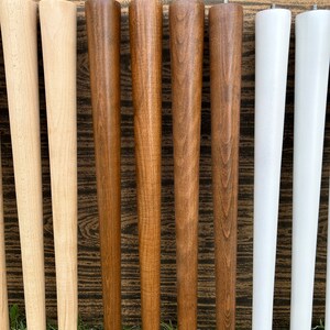 May include: Eight wooden table legs in three different colors: natural wood, dark brown, and white. The legs are tapered and have a smooth finish.