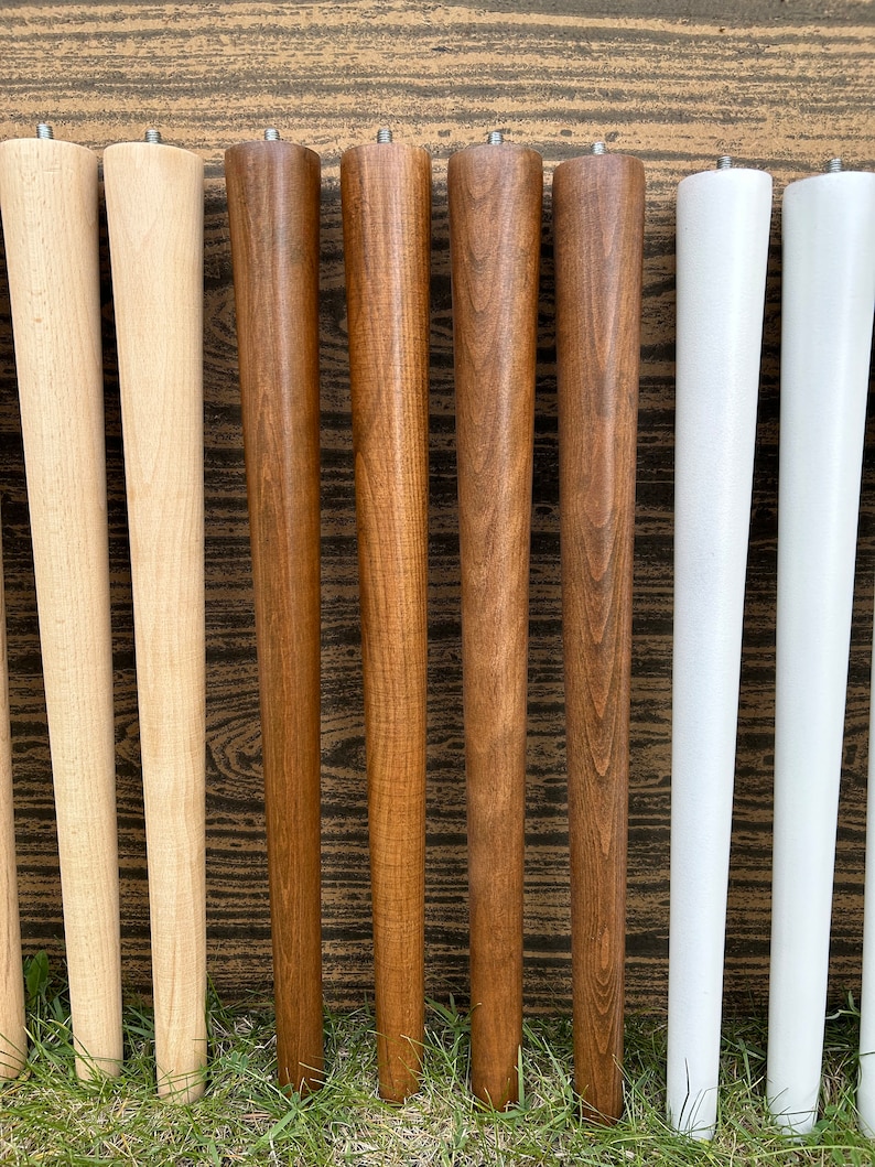 May include: Eight wooden table legs in three different colors: natural wood, dark brown, and white. The legs are tapered and have a smooth finish.
