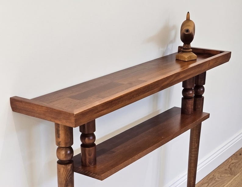 May include: A dark brown wooden console table with two shelves and turned legs. A decorative wooden bird sculpture sits on the top shelf. The table has a rectangular shape and is made of solid wood.