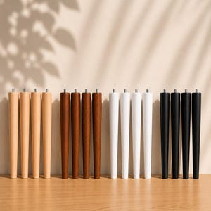 Puede incluir: Dieciséis patas de mueble cónicas dispuestas en cuatro grupos de cuatro, con acabados en madera clara, madera marrón media, blanco y negro. Cada pata es cilíndrica, se estrecha hacia la base e incluye un perno roscado de metal en la parte superior.
