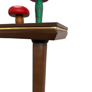 Puede incluir: Una mesa de madera con un borde dorado y una pata de madera marr&oacute;n. Dos figuritas de hongos de madera est&aacute;n encima de la mesa. Un hongo es rosa con flores amarillas y el otro es rojo con puntos blancos.