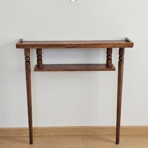 May include: A dark brown wooden console table with a rectangular top and a lower shelf. The table has four slender legs and decorative turned supports. The table is approximately 36 inches long and 30 inches high.