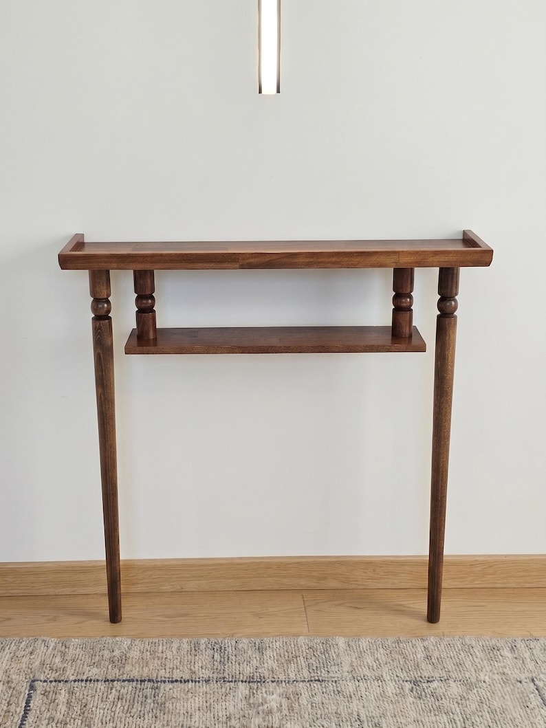 May include: A dark brown wooden console table with a rectangular top and a lower shelf. The table has four slender legs and decorative turned supports. The table is approximately 36 inches long and 30 inches high.