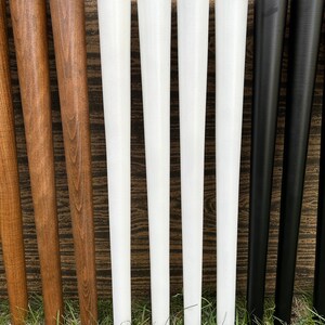 May include: Eight wooden table legs in various colors, including natural wood, white, and black. The legs are all the same size and shape, and they are arranged in a row.