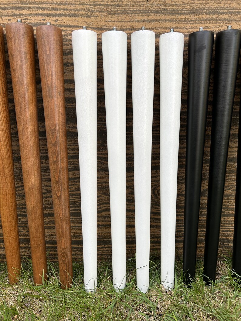 May include: Eight wooden table legs in various colors, including natural wood, white, and black. The legs are all the same size and shape, and they are arranged in a row.