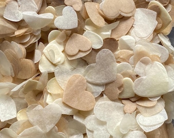 May include: A close-up shot of a pile of heart-shaped confetti. The confetti is in various shades of white, cream, and tan. The hearts are made of a thin, translucent material, creating a delicate and airy appearance. The confetti is scattered, creating a textured and layered effect.