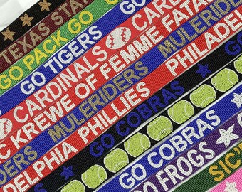 May include: A close-up of ten colorful beaded straps with various team names and logos, including "Go Tigers", "Go Cobras", "Go Frogs", and "Sic'em".