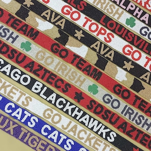 May include: A close-up of ten colorful beaded straps with various college team names and logos. The straps feature text such as "Go Irish", "Go Tops", "Go Team", "SDSU Aztecs", "Chicago Blackhawks", "Go Jackets", "Ohhhhh Cats", "Geaux Tigers", "IU Hoosier", "Kappa Alpha", "Louisville Cardinals", and "Go Irish".
