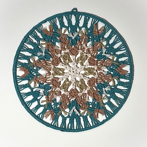 May include: A teal, brown, and white macrame wall hanging with a circular design. The macrame is made with knotted cords and has a fringe around the edge.