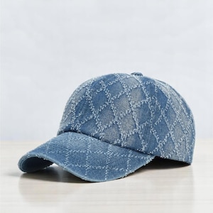 Può includere: Un berretto da baseball in denim blu con un motivo geometrico. Il berretto ha un aspetto leggermente usurato.