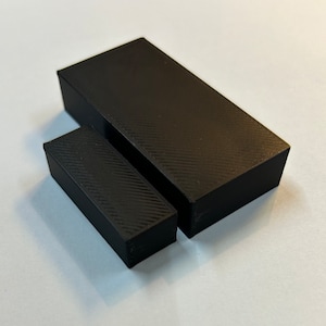 May include: Two black rectangular 3D printed boxes, one is larger than the other.