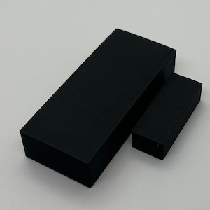 May include: Two black rectangular boxes, one larger than the other, are shown on a white surface. The boxes are made of a textured material.