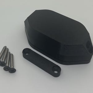 May include: A black, geometric object with a matching black bracket and four silver screws. The object has a textured surface and appears to be 3D-printed. The bracket has two holes for mounting.