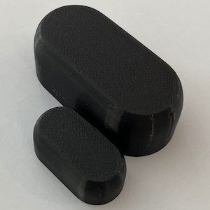May include: Two black oval-shaped plastic objects. The larger object is on top of the smaller object.
